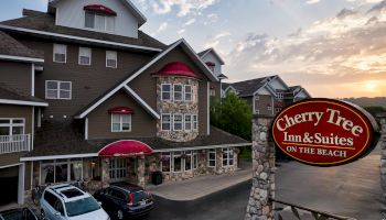 The image shows Cherry Tree Inn & Suites, a hotel located on the beach. There are cars parked in front and a sign displaying the hotel's name.