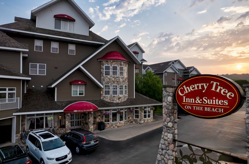 The image shows Cherry Tree Inn & Suites, a hotel located on the beach. There are cars parked in front and a sign displaying the hotel's name.