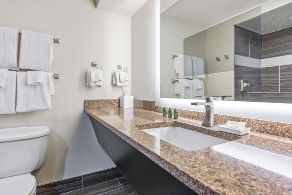 A bathroom with a granite countertop, sink, modern faucet, large mirror, neatly hung towels, and a toilet is shown in the image.