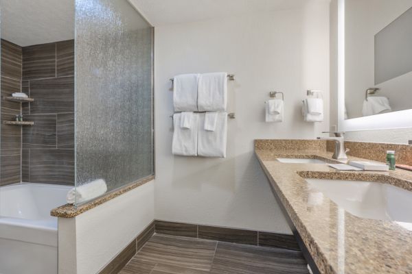 A clean, modern bathroom with a granite countertop, sink, bathtub with glass partition, wall-mounted towel racks with towels, and a mirror.