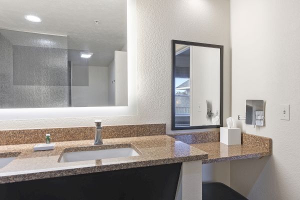 A bathroom with a granite countertop, sink, illuminated mirror, tissue box, and an installed hairdryer on the right wall ends the sentence.