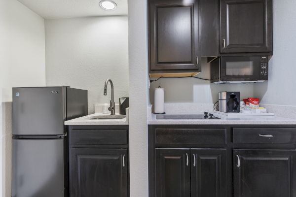 A compact kitchen setup with dark cabinets, a mini refrigerator, microwave, sink, stovetop, coffee maker, and paper towel holder on the counter.