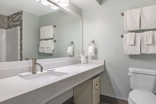 A modern bathroom with a large mirror, white countertop sink, toilet, and neatly hung towels on the wall.