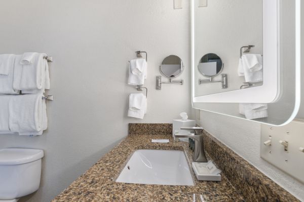 The image shows a clean, modern bathroom with a granite countertop, a rectangular sink, wall-mounted mirrors, and neatly arranged towels.