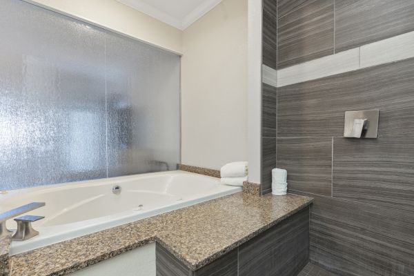 A modern bathroom features a large bathtub with a granite countertop, adjacent to a tiled shower area with a glass screen for privacy.