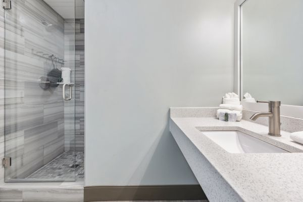 The image shows a modern bathroom with a glass-enclosed shower, a countertop with a sink, a faucet, and neatly arranged towels.