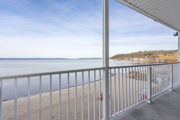 A balcony view overlooking a sandy beach and calm sea, with a railing in the foreground and a clear sky above.