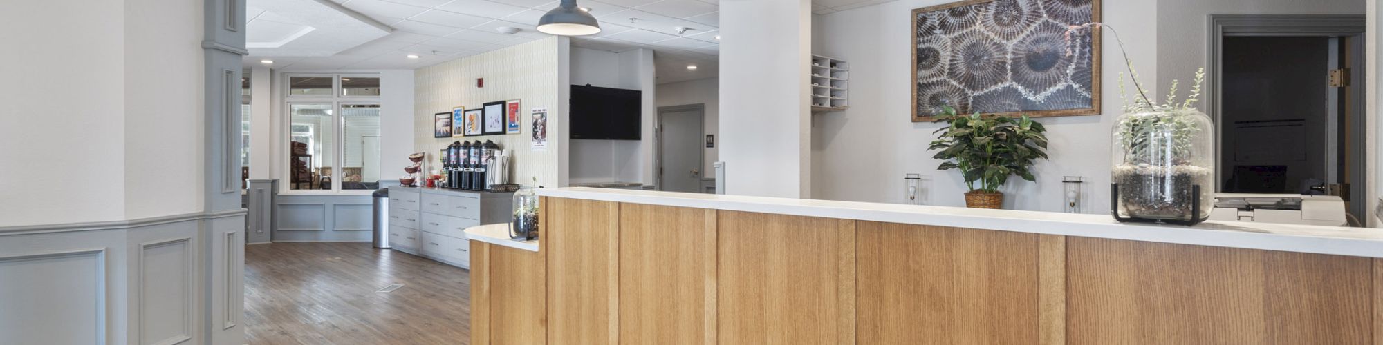 The image shows a reception area with a wooden counter, pendant lights, and a potted plant. There is a seating area in the background.