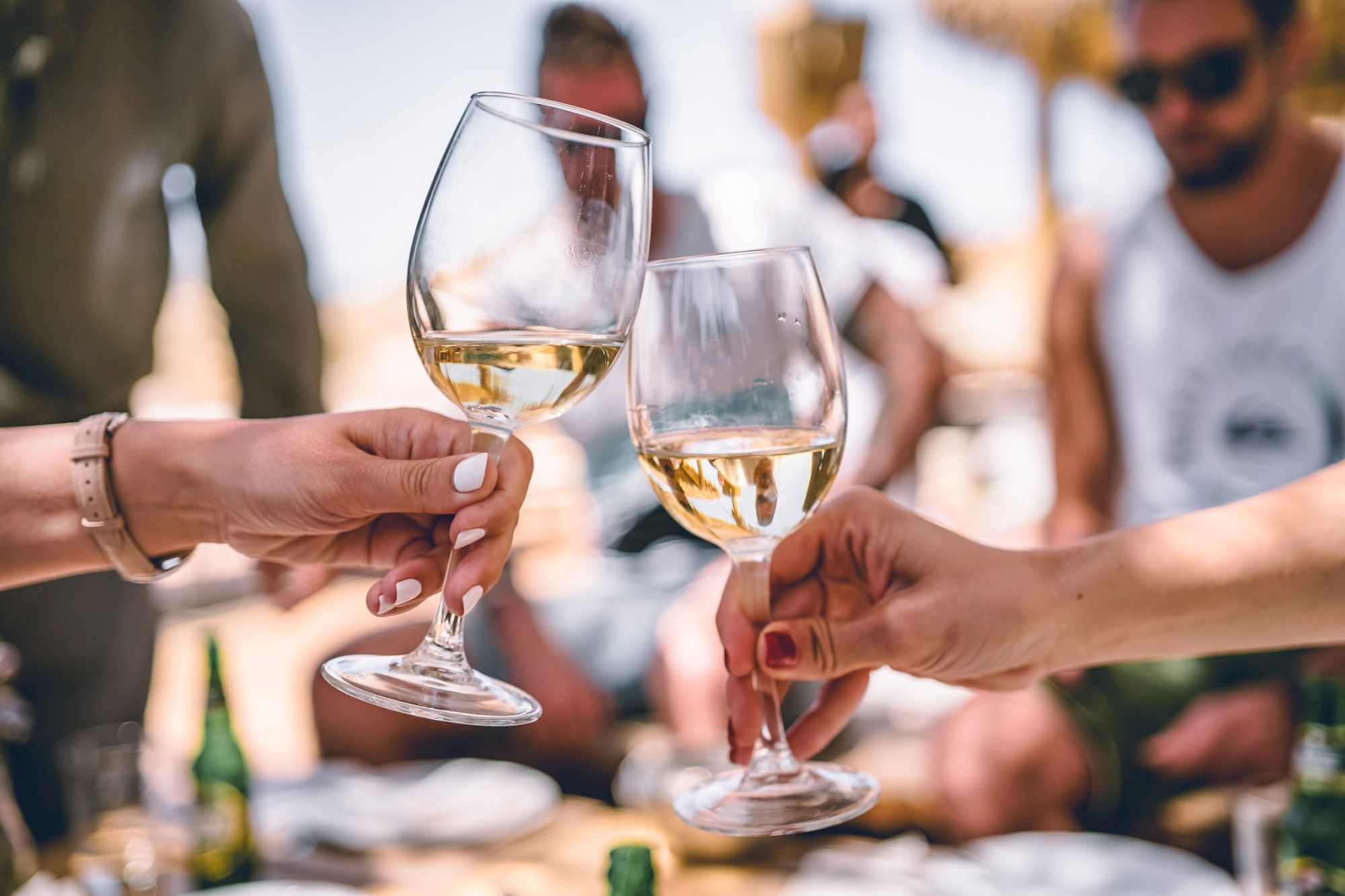 Two people clinking wine glasses in a celebratory toast, with others blurred in the background.