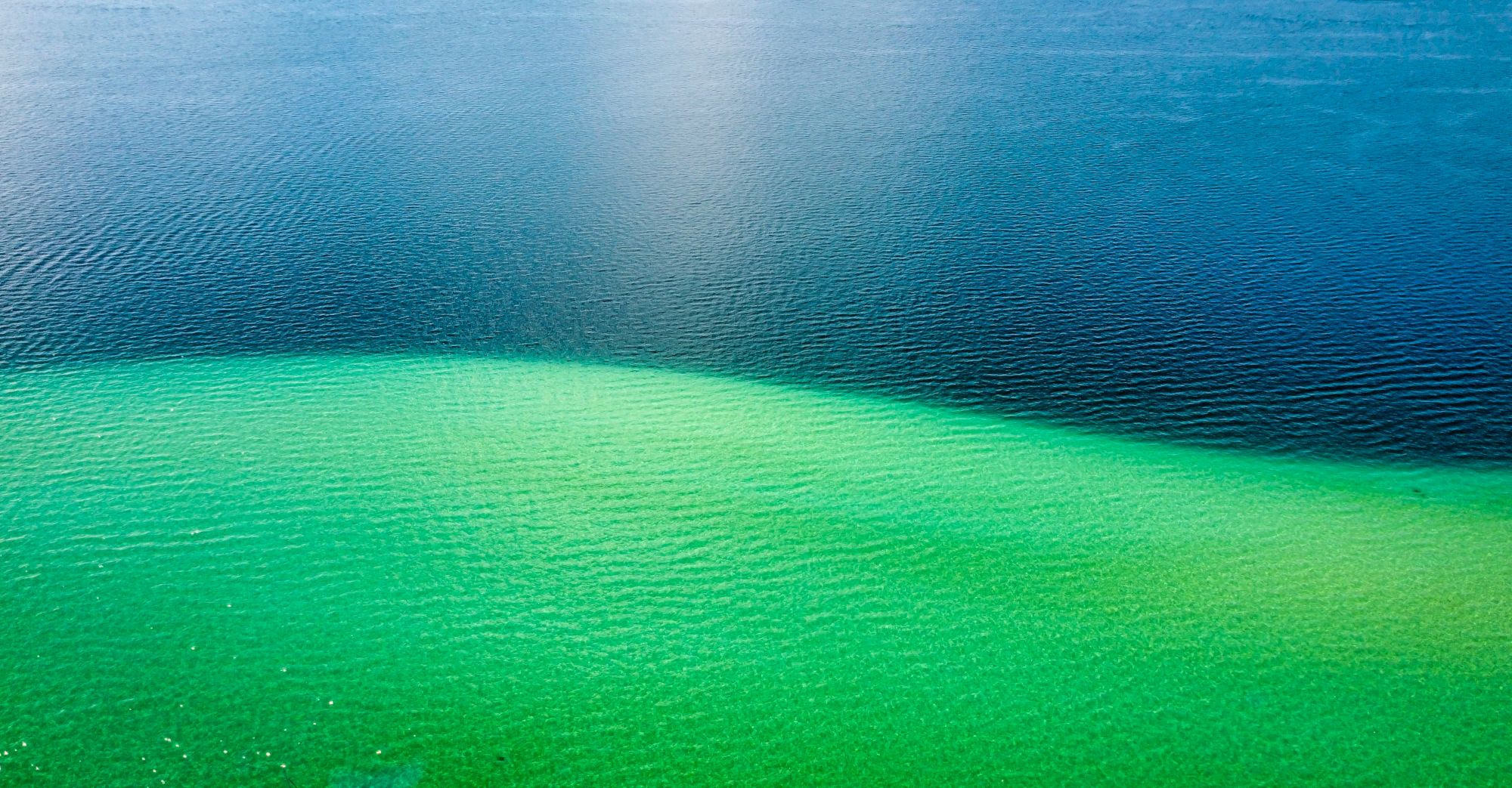 The image shows a body of water with a gradient color transition from deep blue at the top to bright green at the bottom, creating a striking contrast.