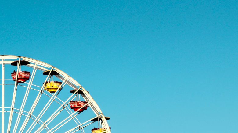 The image shows a partial view of a Ferris wheel against a clear blue sky, with red and yellow gondolas.