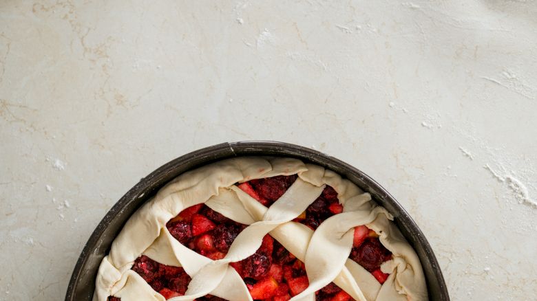 A fruit pie with a lattice crust in an unbaked state, placed on a light-colored surface.