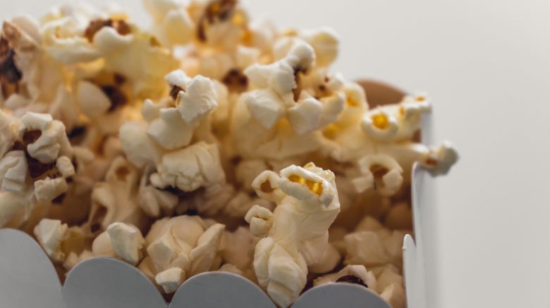 The image shows a close-up of freshly popped popcorn in a white cardboard container.