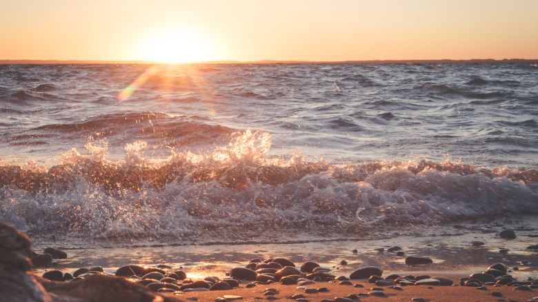 The image shows a serene beach scene with gentle waves, a pebbled shore, and a beautiful sunset casting a warm glow over the water.