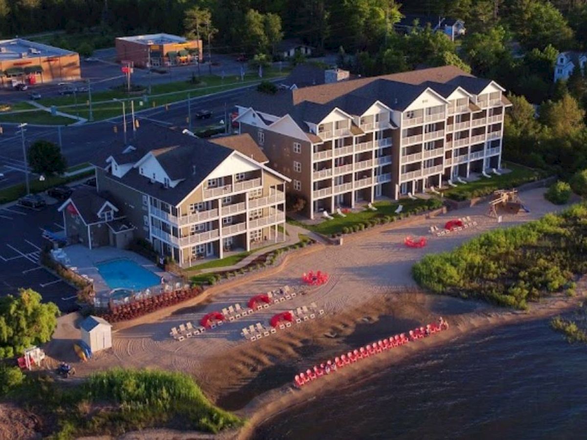 The image shows a lakeside resort with a pool, beach chairs, umbrellas, and several buildings behind it amidst lush greenery.