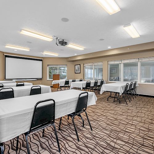 A well-lit conference room with rows of tables and chairs, a projector, and large windows, all set up for a meeting or presentation.