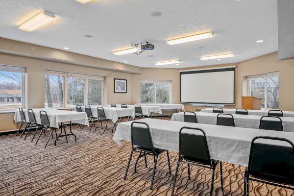 The image shows a conference room with tables and chairs, a projector, and a projection screen. Natural light enters through multiple windows.