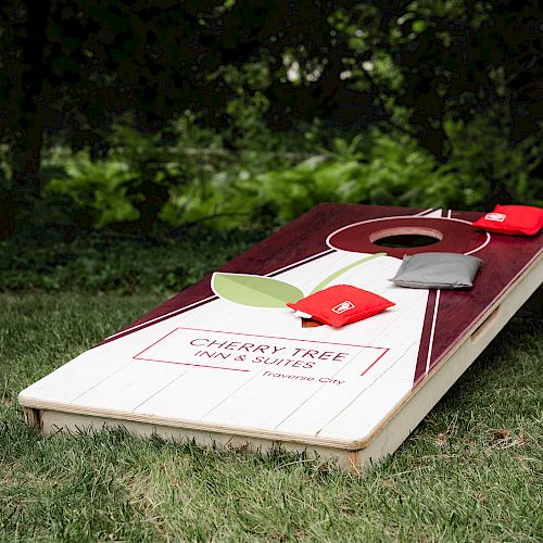 A cornhole board with bean bags on grass. The board reads 