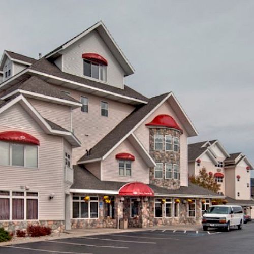 A multi-story inn with peaks and dormers, featuring a red awning and sign reading "Cherry Tree Inn & Suites." An American flag is seen.