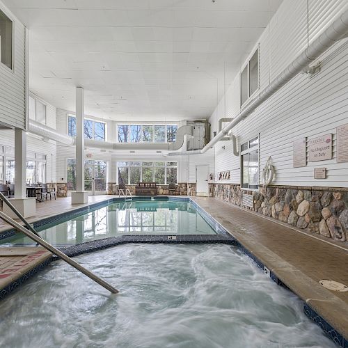 An indoor pool area featuring a whirlpool and a standard swimming pool, with large windows letting in natural light.