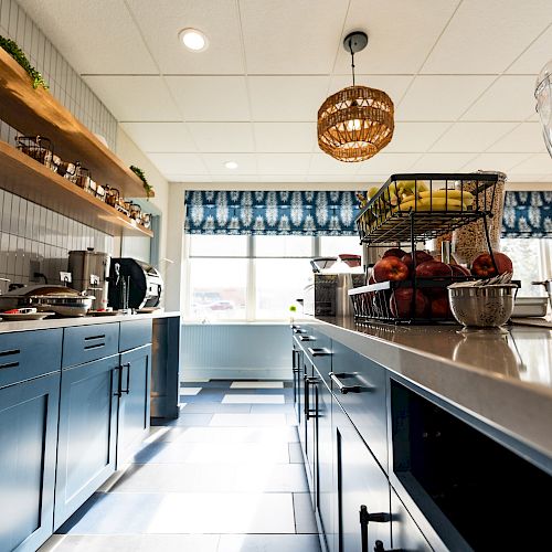 This image shows a modern kitchen with blue cabinets, a tiled floor, and a large counter with various kitchenware and fresh pomegranates on display.