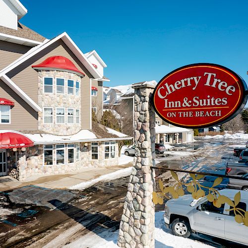 The image shows a hotel named Cherry Tree Inn & Suites on the Beach, with a snowy landscape and parked cars outside the building.