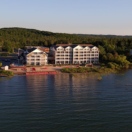 The image depicts a waterfront area with multi-story buildings and greenery in the background, situated next to a body of water reflecting the sunlight.