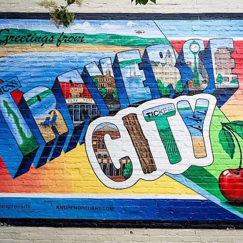 A colorful mural on a brick wall reads "Greetings from Traverse City," featuring cherries and various landmarks.