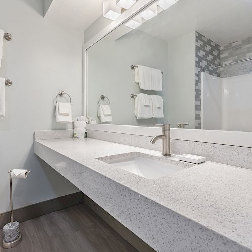 A modern bathroom with a sink, large mirror, toilet, and towels on racks next to a shower area with a tiled wall and curtain ending the sentence.