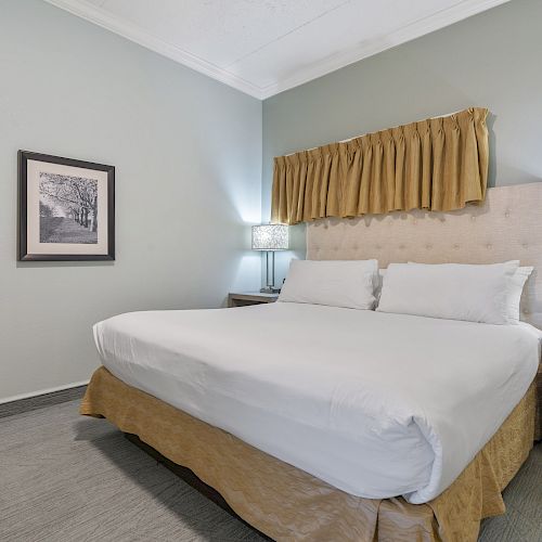 This image shows a neatly made bed in a hotel room with two bedside tables, lamps, and a framed picture on the wall.