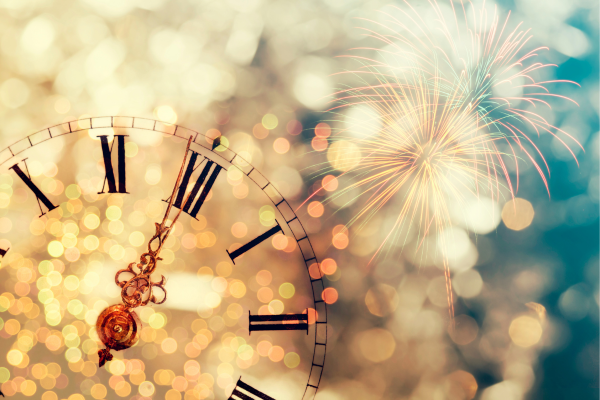 A clock nearing midnight with bokeh lights and fireworks in the background creates a festive New Year's Eve atmosphere.