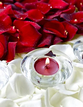 Red and white rose petals with three lit red tea light candles in glass holders.