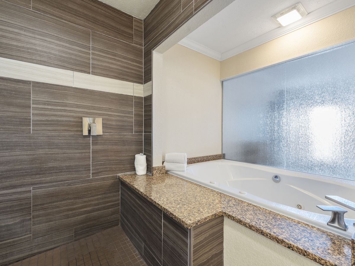 A modern bathroom with a large bathtub, granite countertops, tiled walls, and a frosted glass window for privacy.