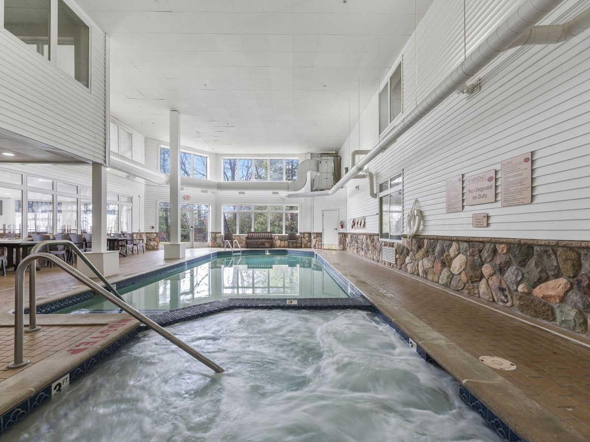 An indoor pool area with a hot tub in the foreground, surrounded by windows, stone walls, and white paneling.