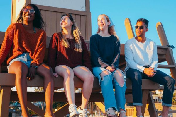 Four people are sitting on a wooden structure outdoors, smiling and enjoying the sunny weather.