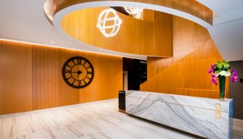 A modern reception with wooden decor, a marble desk, a large wall clock, and decorative lighting hanging from the ceiling ends the sentence.