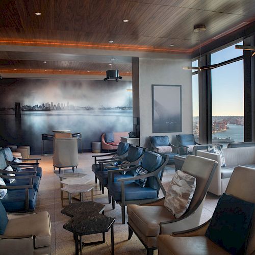A modern lounge with ample seating, large windows offering a scenic view, a mural of a city skyline, and minimalist decor.