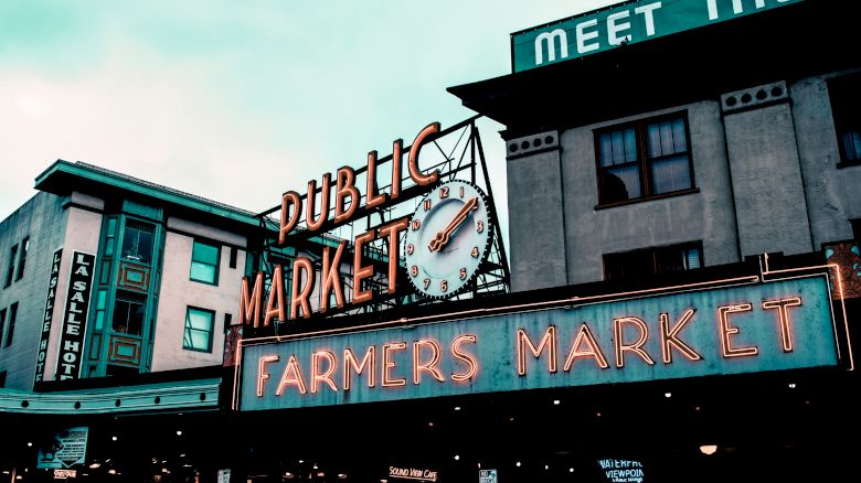 The image shows the iconic neon signs for "Public Market" and "Farmers Market" at the entrance of Pike Place Market in Seattle, Washington.